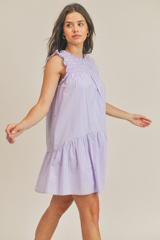 Lavender sleeveless dress with smock neck, ruffle hem and side pocket detail.