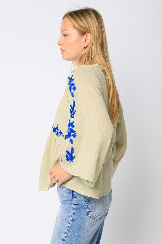 Cotton woven light green peasant top with dolman sleeves, button down back, and royal blue floral embroidered pattern.
