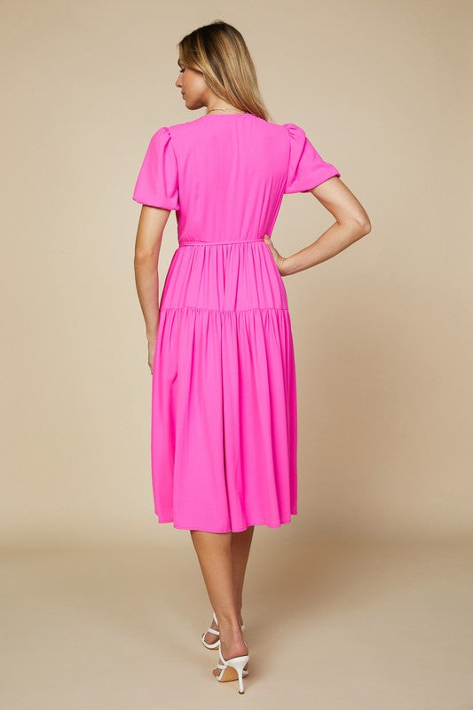 Neon pink maxi dress with a fitted wrap top, puff sleeves, and tiered skirt.