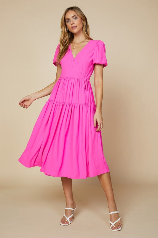Neon pink maxi dress with a fitted wrap top, puff sleeves, and tiered skirt.