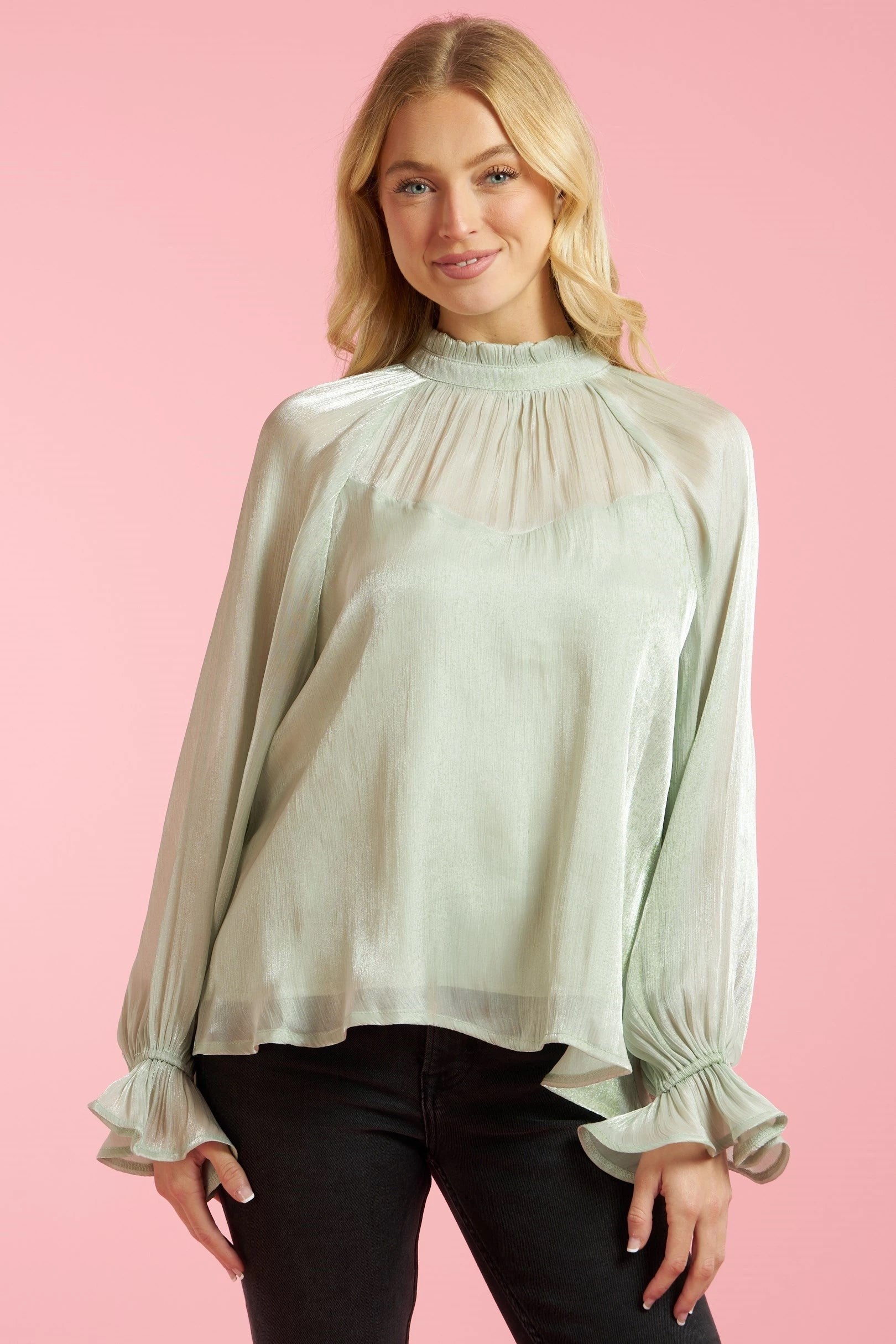 Sage green long sleeve blouse with sheer top and sleeve contrast, ruffle cuffs, high neck, button close back, and shimmer finish.